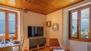 A cozy living room with a TV, wooden furniture, and large windows offering a mountain view. - Rimaye Blanche - A bright and cozy 1 bed apartment. (Chamonix-Mont-Blanc)