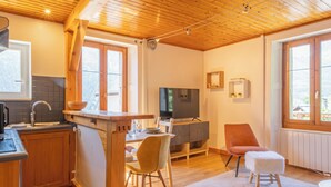 A cozy cabin interior with a wooden ceiling, a kitchen area with a sink and stove, a dining table with chairs, a television, and a cozy seating area with a chair and ottoman. - Rimaye Blanche - A bright and cozy 1 bed apartment. (Chamonix-Mont-Blanc)
