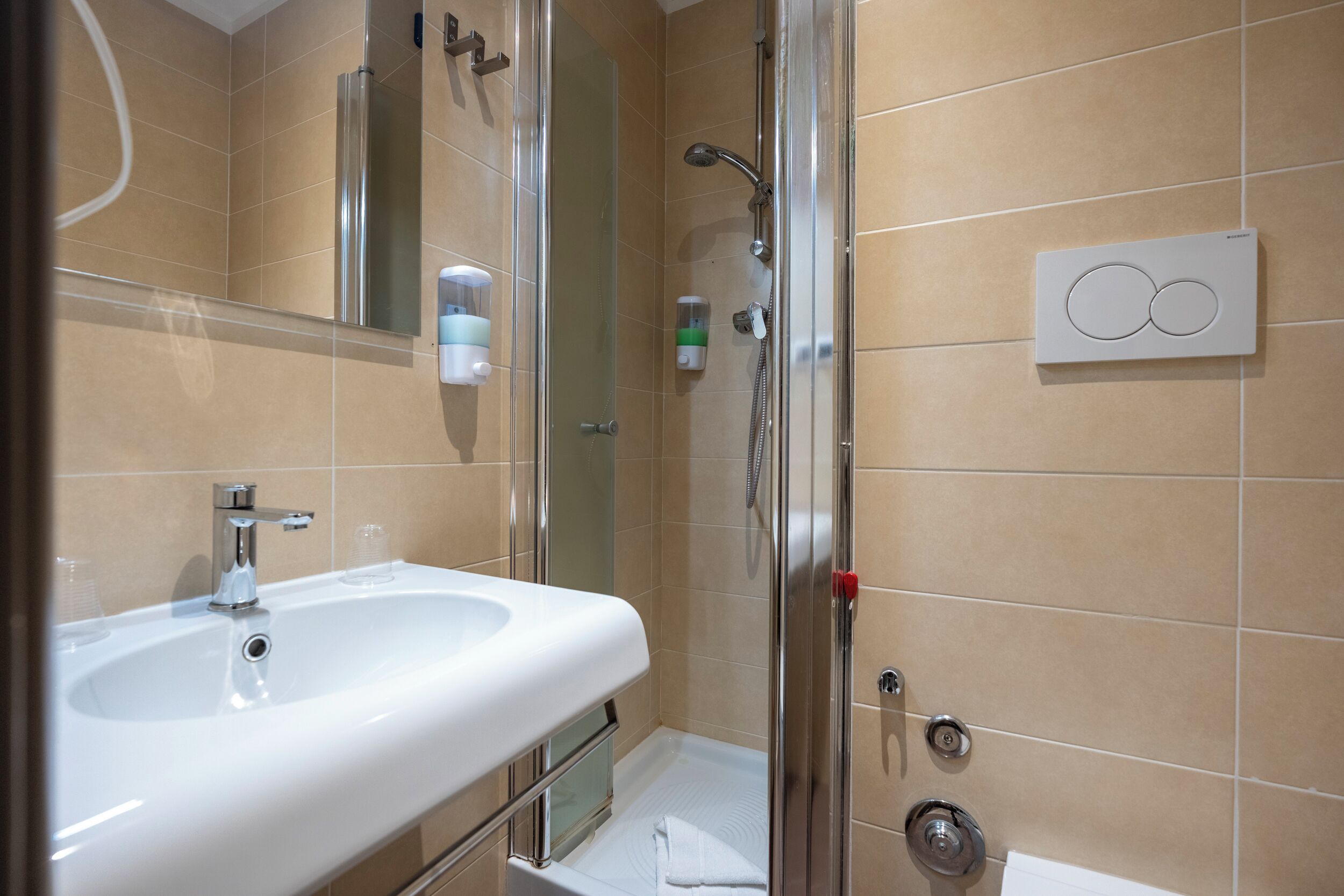 Un baño moderno con lavamanos, espejo, ducha y un panel de control en la pared.