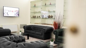 Sala de estar com sofá preto, mesa de centro de vidro, televisão de tela plana e aparador com figurines.