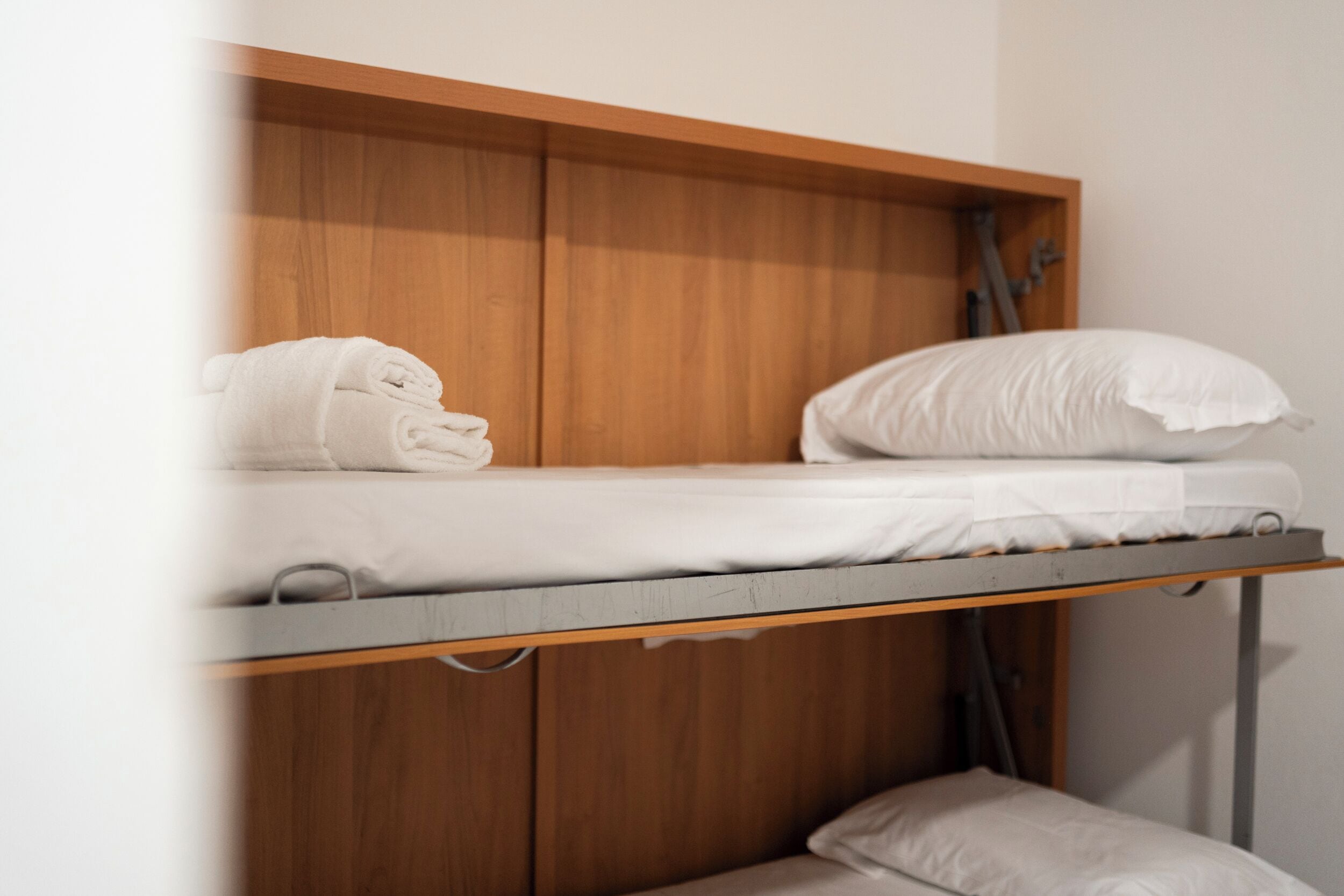 A bunk bed with a wooden headboard, a white pillow, and a rolled-up towel on the top bunk.