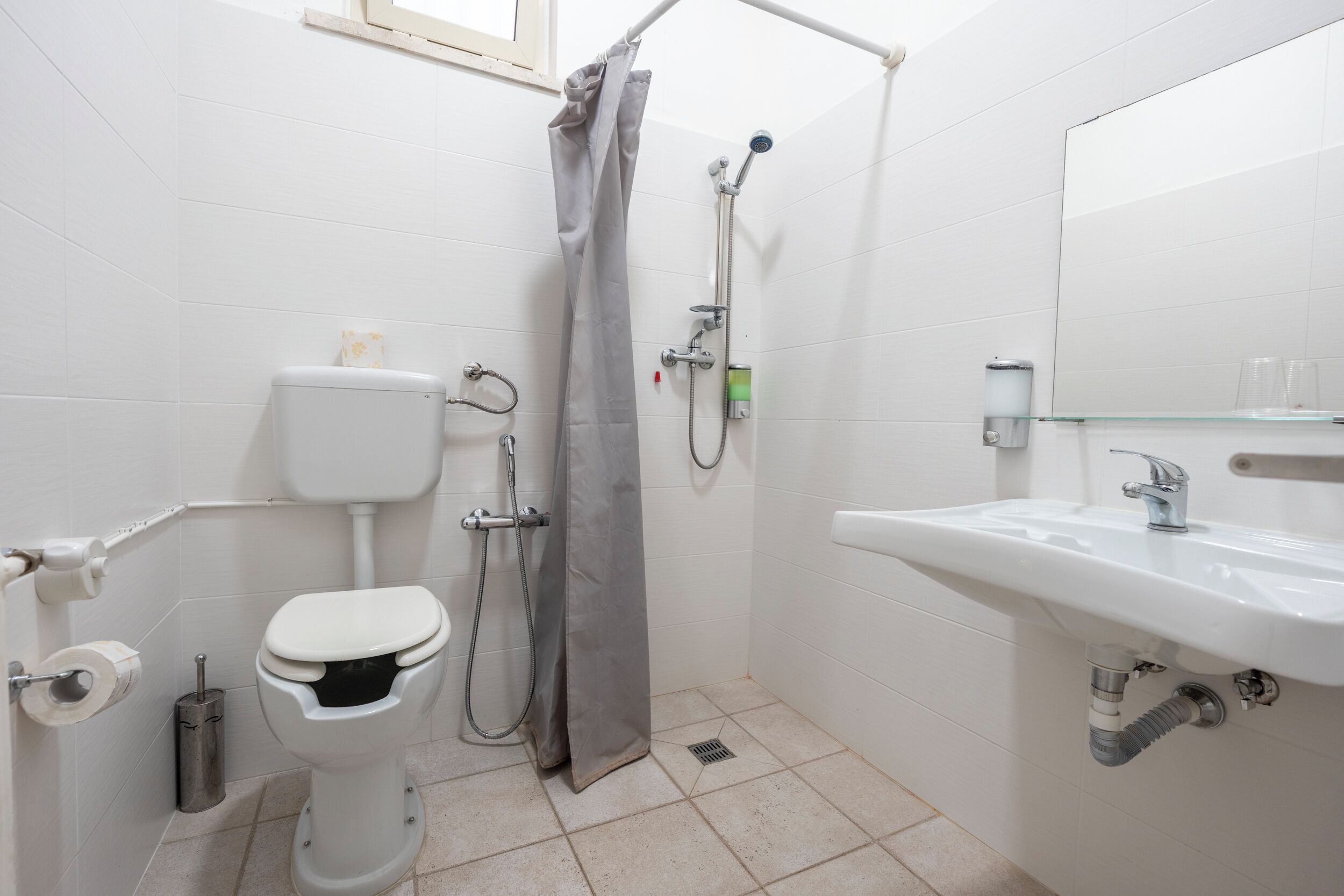 A bathroom with a toilet, shower, sink, and mirror.