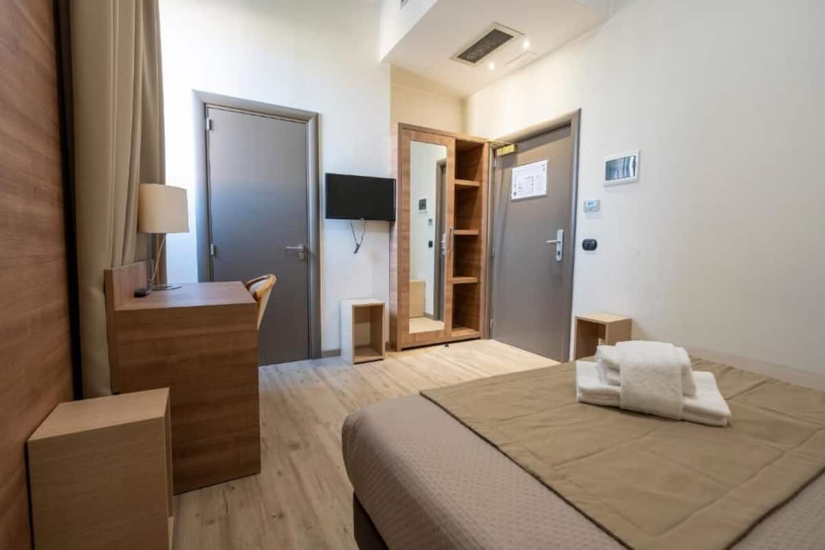Ett hotellrum med en säng, ett skrivbord, en tv och en garderob.