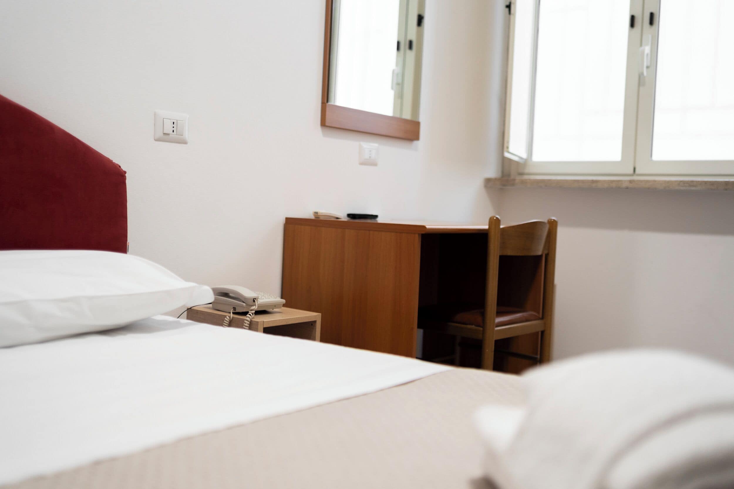 Une chambre d’hôtel avec un lit, un bureau avec un téléphone, une chaise et une fenêtre.