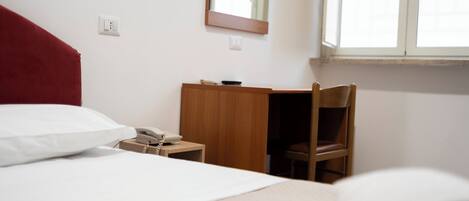 Une chambre d’hôtel avec un lit, un bureau avec un téléphone, une chaise et une fenêtre.