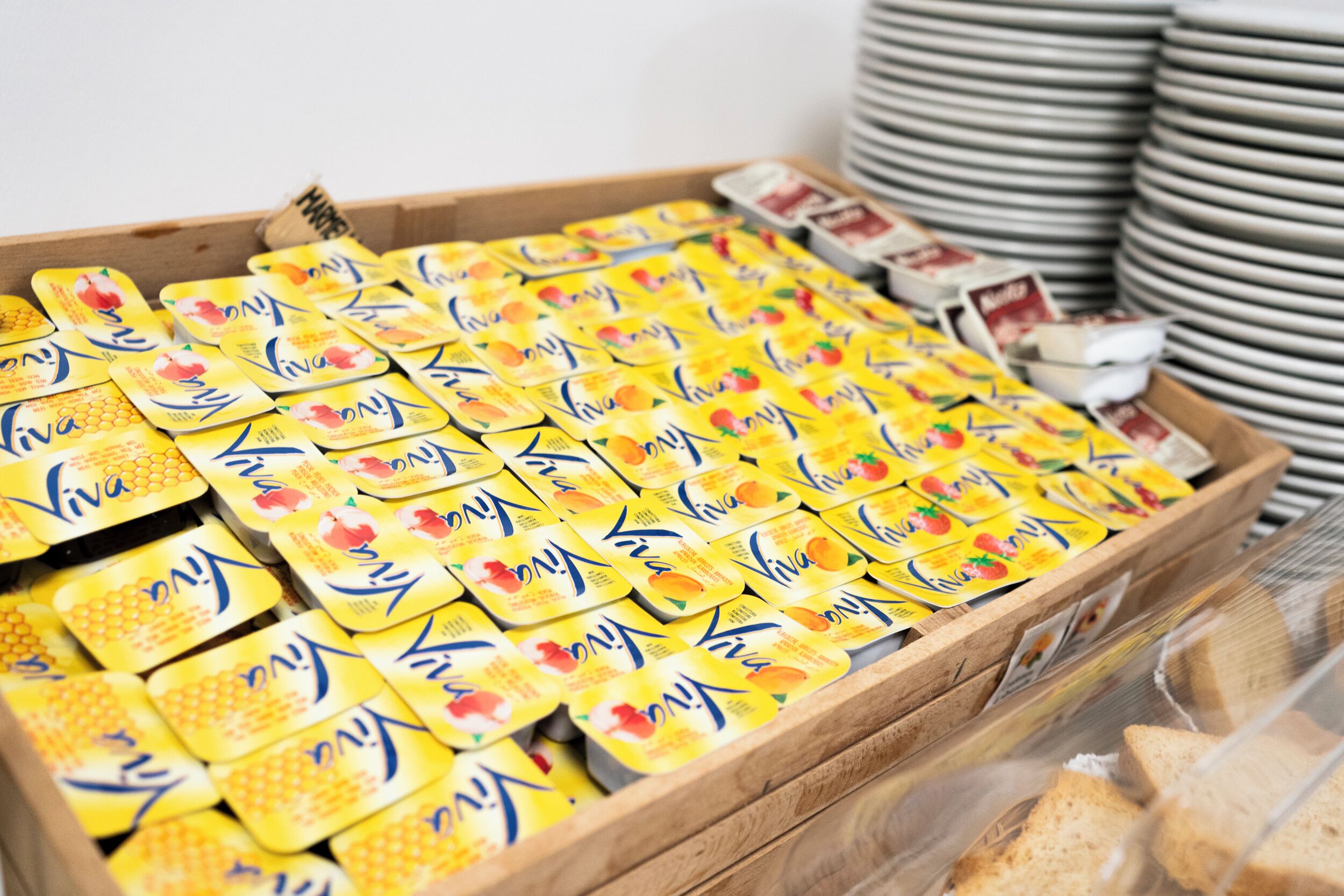 A wooden crate filled with yellow boxes labeled 'Viva' and a stack of white plates in the background.