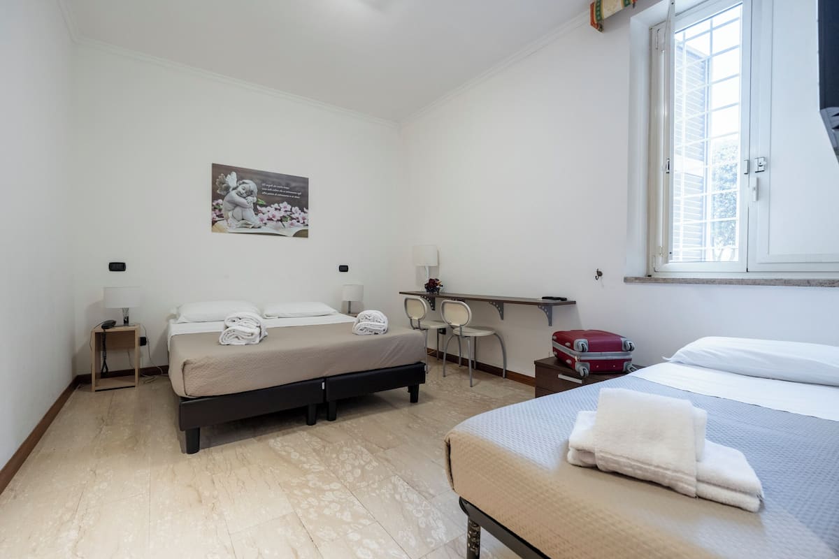 Ett hotellrum med två sängar, ett skrivbord med stolar, ett fönster och en tavla som hänger på väggen.