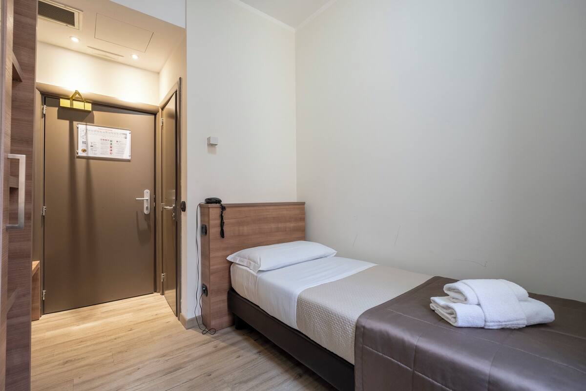 Ett hotellrum med en säng, en sänggavel i trä, en dörr med en skylt och en handduk på sängen.