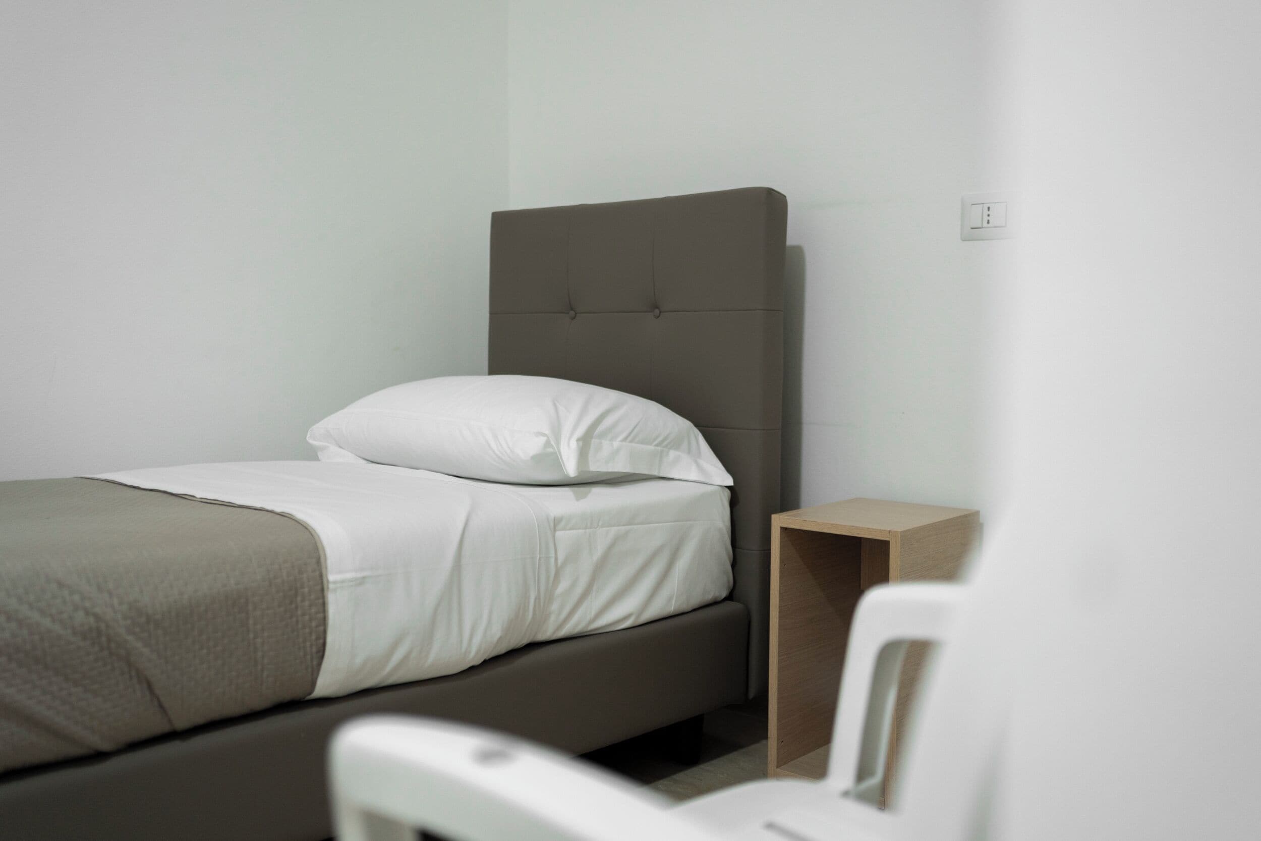 Ein Einzelbett mit Kopfstütze, einem Nachttisch und einer Steckdose.