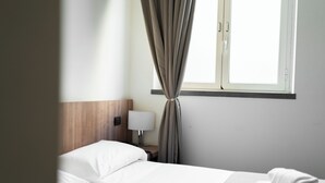 Quarto de hotel com uma cama, mesa de cabeceira, abajur e janela com cortinas.