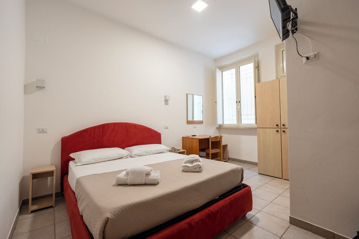 Ett hotellrum med en säng, ett skrivbord, en garderob och en tv som är monterad på väggen.