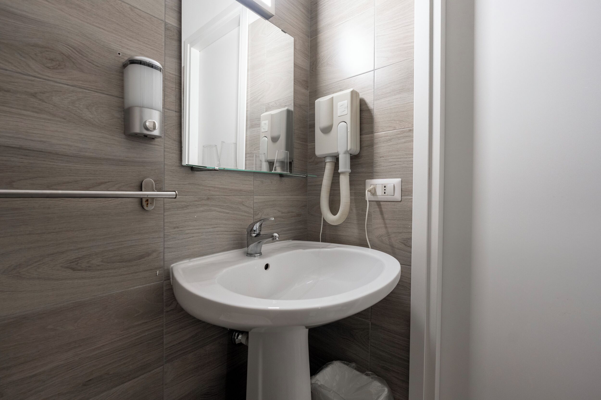 A bathroom with a white sink, a mirror, a towel rack, and a hand dryer.
