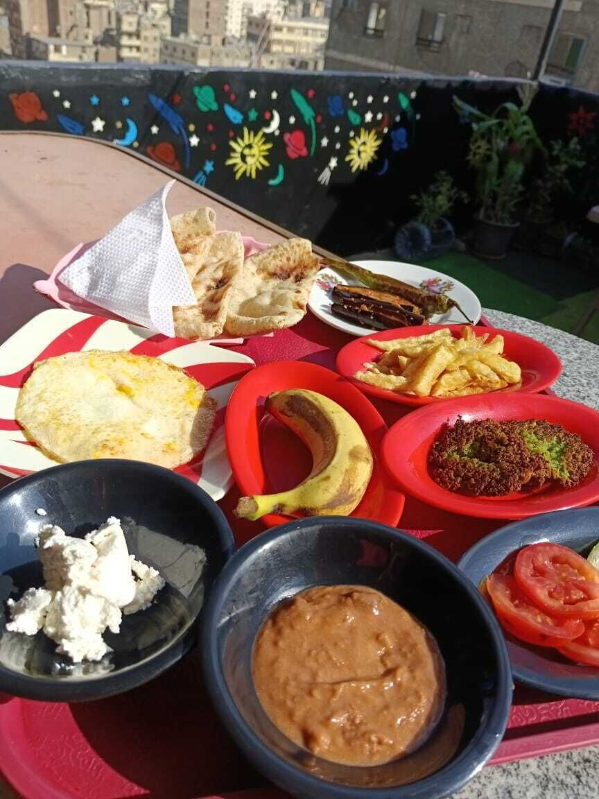 Une table dressée à l’extérieur, avec divers plats, notamment du pain, des frites et des sauces, et en arrière-plan, une vue sur la ville.