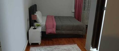 A bedroom with a bed, bedside table, lamp, and a window with curtains.