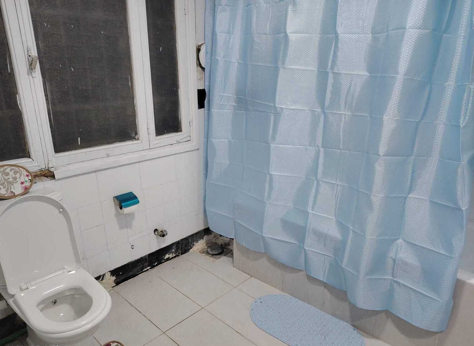 A bathroom with a toilet, a window, and a blue shower curtain.