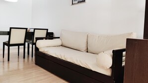 Een minimalistische woonkamer met een bank, twee fauteuils, een bijzettafeltje en een lijst met een foto aan de muur.