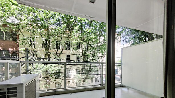 Een balkon met uitzicht op bomen en gebouwen, een raam en een airconditioning.
