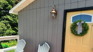 A porch with two white Adirondack chairs, a lantern, and a door with a wreath.