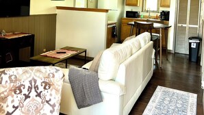 A compact living space with a sofa, a small table, a TV, and a kitchenette.