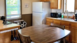 A compact kitchen with wooden cabinets, a white refrigerator, a stove, and a dining table with chairs.