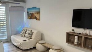 A modern living room with a sofa, a flat-screen TV, and a wooden shelf. - Relaxing Studio Near El Yunque With Pool View (Luquillo)