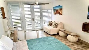 A bedroom with a bed, a sofa, a small table, and a painting on the wall. - Relaxing Studio Near El Yunque With Pool View (Luquillo)