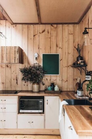 A kitchen with wooden walls, a microwave, cabinets, a potted plant, and a chalkboard.