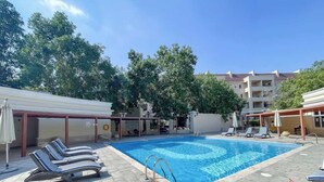 Una piscina con sillas de descanso y sombrillas, rodeada de edificios y árboles.