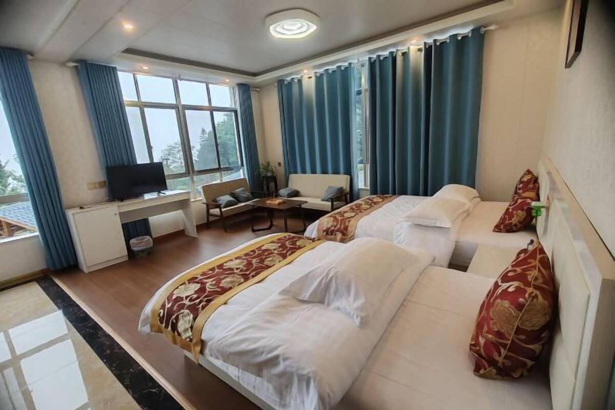 A hotel room with two beds, a desk with a TV, a chair, and large windows with curtains.