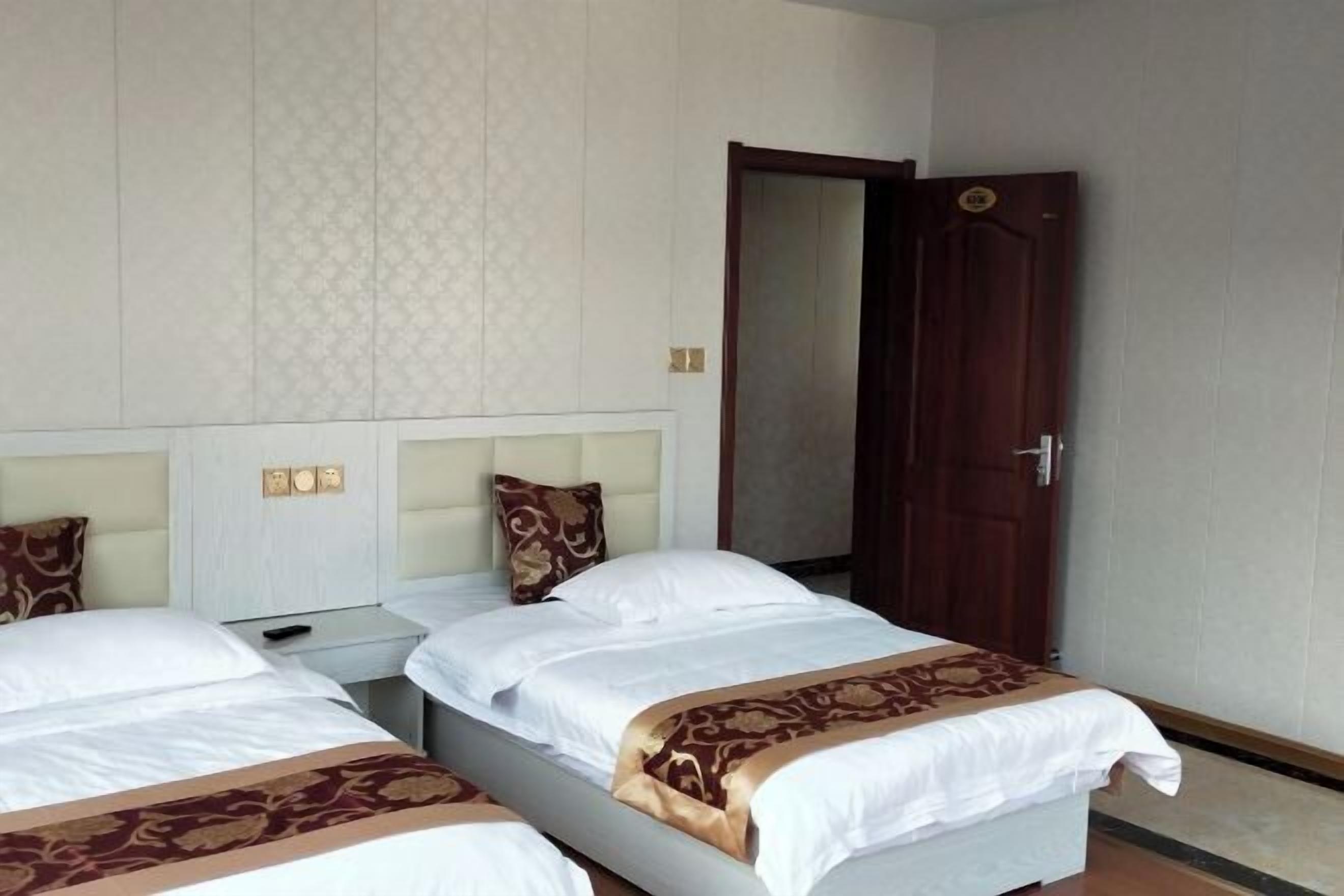 Habitación de hotel con dos camas, una puerta de madera y un papel tapiz estampado.