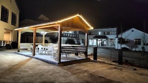 Un kiosque en bois doté d’un toit, illuminé par des guirlandes lumineuses, et entouré d’un sol en béton.