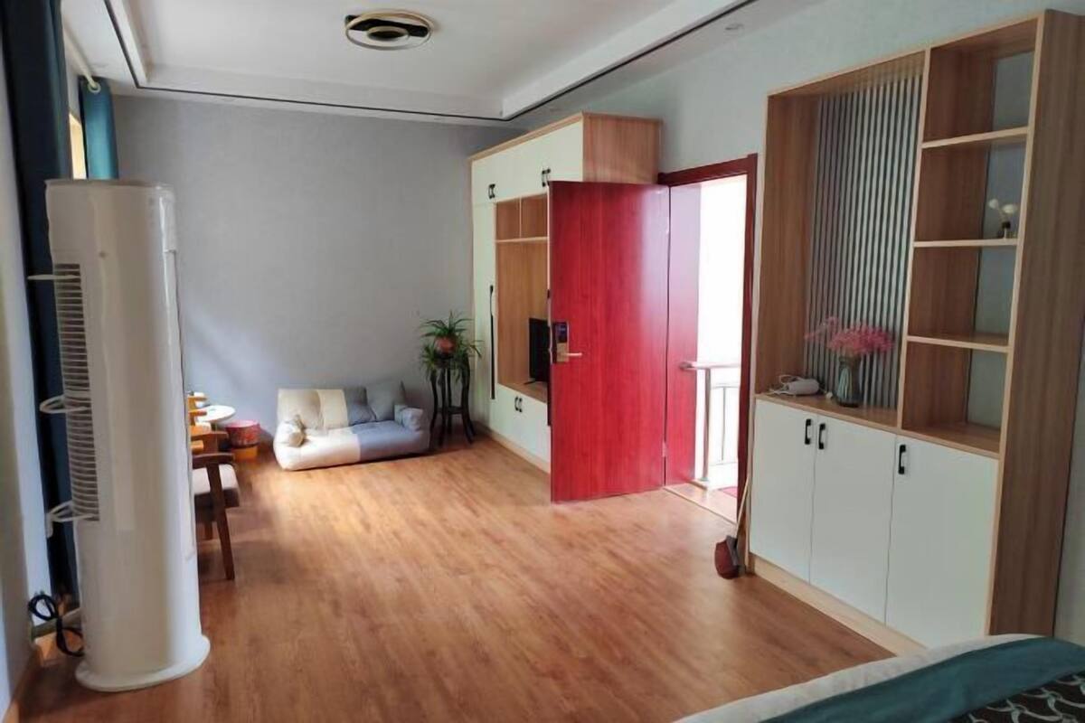 A bedroom with a bed, a wardrobe, a TV, a plant, and a desk with a chair.