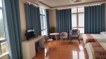 Habitación de hotel con televisión, dos sillas, una mesita, cama y ventanas amplias con cortinas.