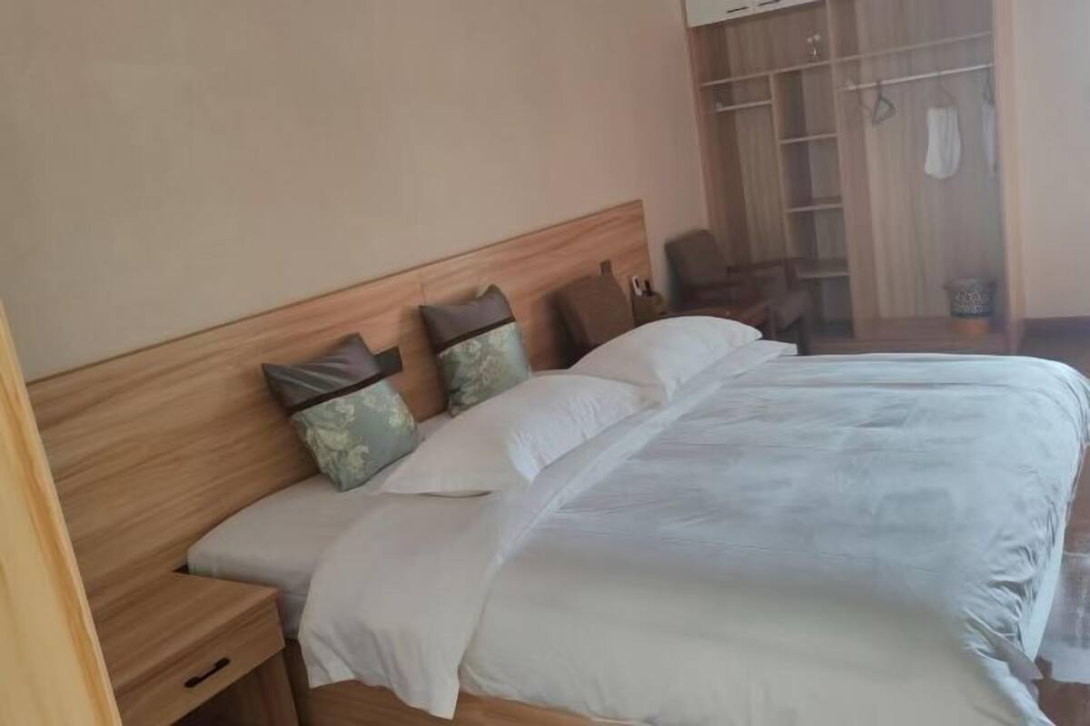 A neatly made bed with a wooden headboard, a bedside table, and a wardrobe with a mirror.