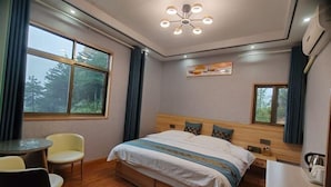 Une chambre d’hôtel avec un lit, une petite table, deux chaises, une fenêtre donnant sur des arbres et un luminaire au plafond.