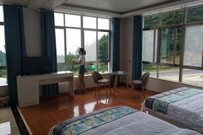 Habitación de hotel con escritorio, dos camas, televisión y ventanas amplias.