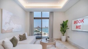 A modern living room with a white sofa, a coffee table, and a large window offering a view of the beach. - StayShort - Cozy 2BR in Palm Jumeirah with Beach Views! (Palm Jumeirah)