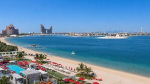 A resort with a pool, beach umbrellas, and a view of the ocean and city skyline. - StayShort - Cozy 2BR in Palm Jumeirah with Beach Views! (Palm Jumeirah)
