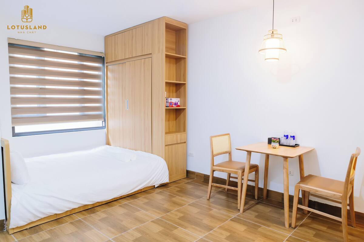 A room with a bed, a wooden wardrobe, a table with chairs, and a hanging light fixture.