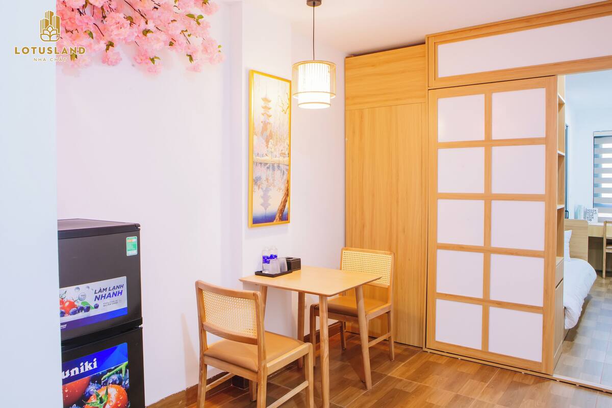 A room with a wooden table and chairs, a refrigerator, a hanging light fixture, and a sliding door.