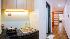 A modern kitchen with a built-in stove, sink, and wooden cabinets. A hallway leads to a traditional dining area. - Lotus Land Apartment (Hanoi)
