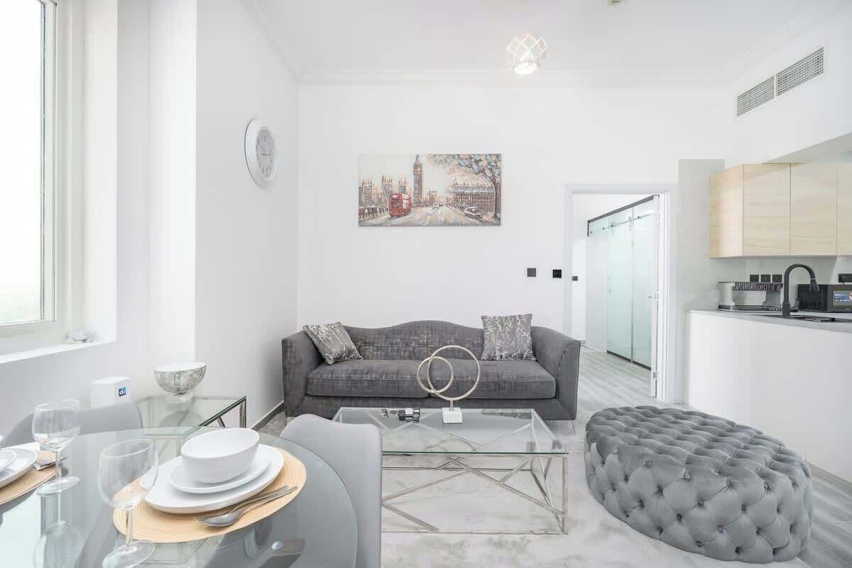 Un salon moderne avec une table basse en verre, un canapé gris et un tableau représentant un paysage urbain.