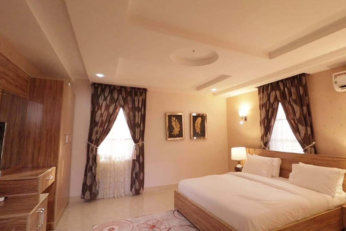 Une chambre d’hôtel avec un lit en bois, deux lampes de chevet, un téléviseur à écran plat et une grande fenêtre avec des rideaux.