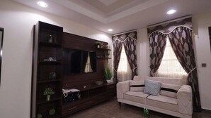 Un salon avec un canapé beige, un meuble de télévision en bois foncé et des rideaux.