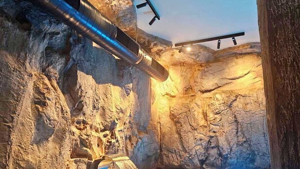 Une piscine intérieure avec un mur en forme de grotte rocheuse et une cascade.