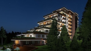 Un hôtel à plusieurs étages, doté de balcons, d’une façade bien éclairée et entouré d’un jardin.