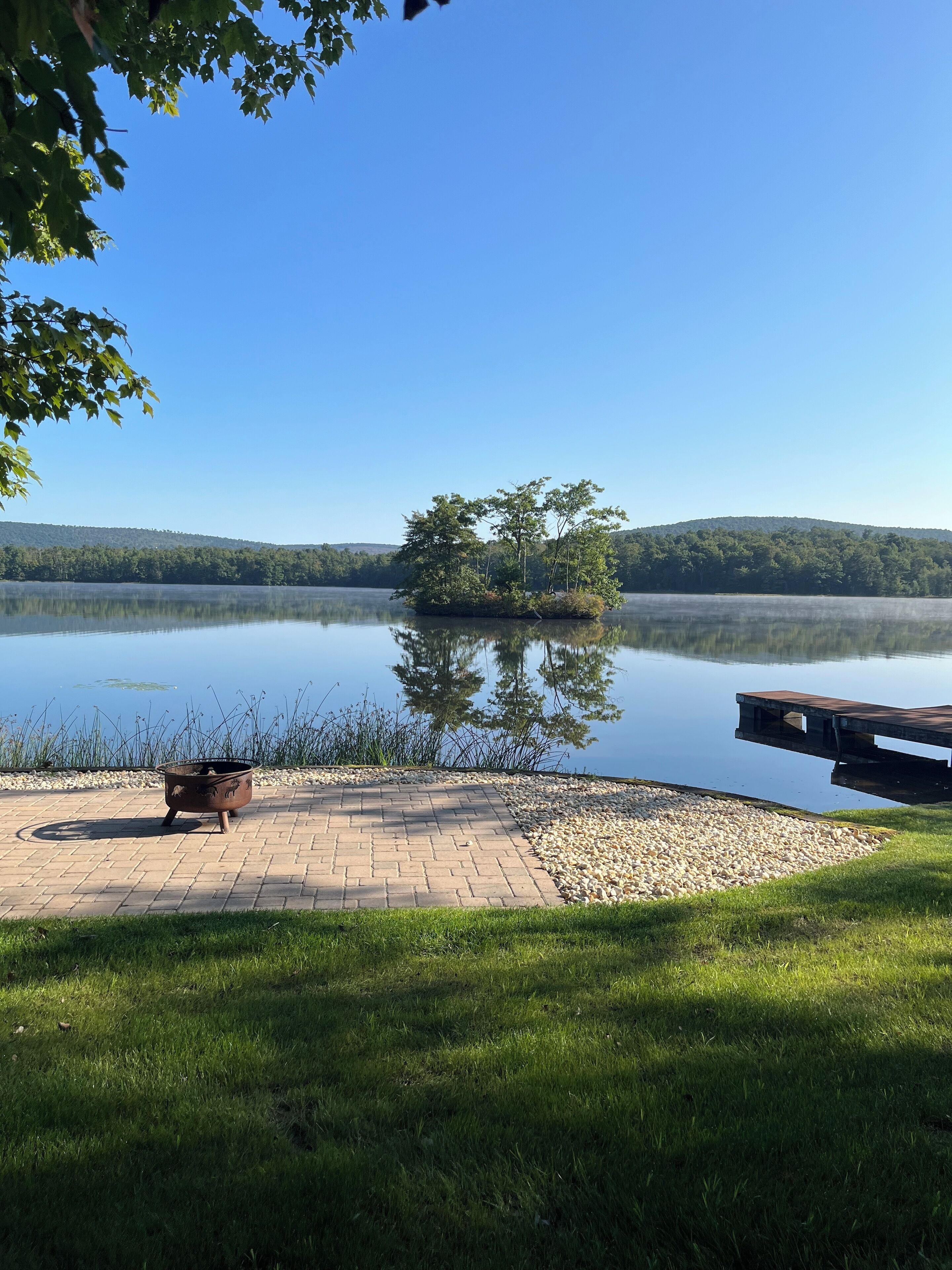 Un cadre paisible au bord du lac, avec une jetée en bois, un chemin pavé de briques et un foyer rustique.
