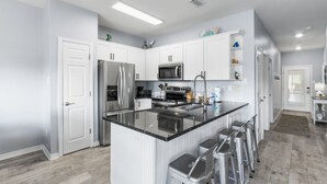 A modern kitchen with white cabinets, stainless steel appliances, and a central island with bar stools. - Romar Lakes 103B w Pool (Orange Beach)