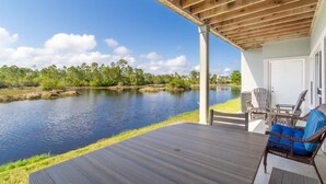 A covered outdoor deck with a view of a calm lake and surrounding greenery. - Romar Lakes 103B w Pool (Orange Beach)