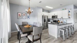 A modern kitchen with white cabinets, stainless steel appliances, and a central island with bar stools. - Romar Lakes 103B w Pool (Orange Beach)